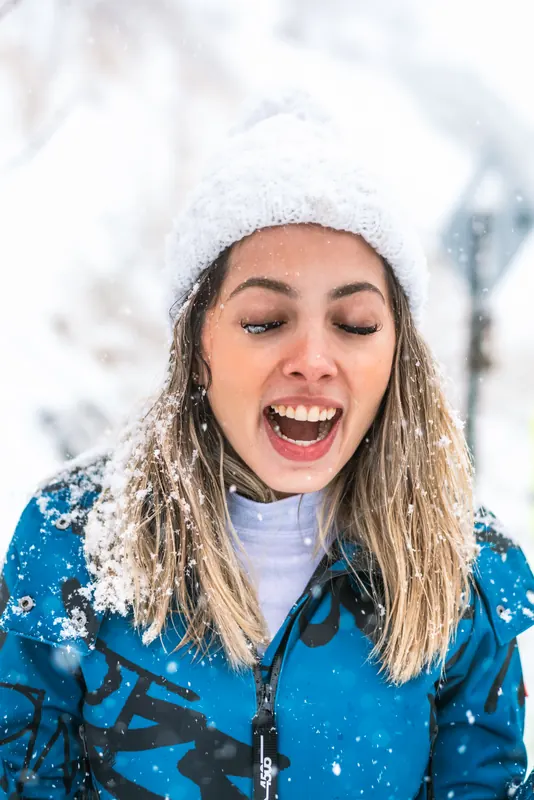 Portrait of Laise laughing in a white knit hat while snow falls