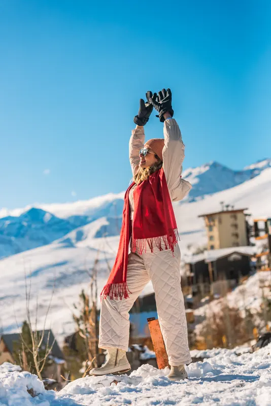 Laise in a red scarf with arms raised in front of snowy mountains