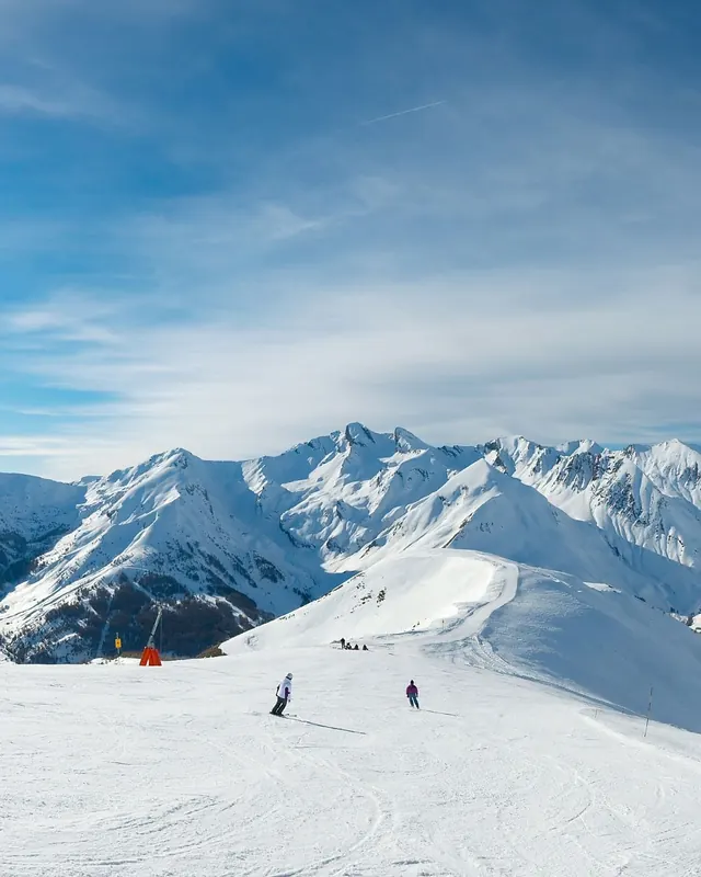 Skiers below snow-covered Andes peaks under a blue sky